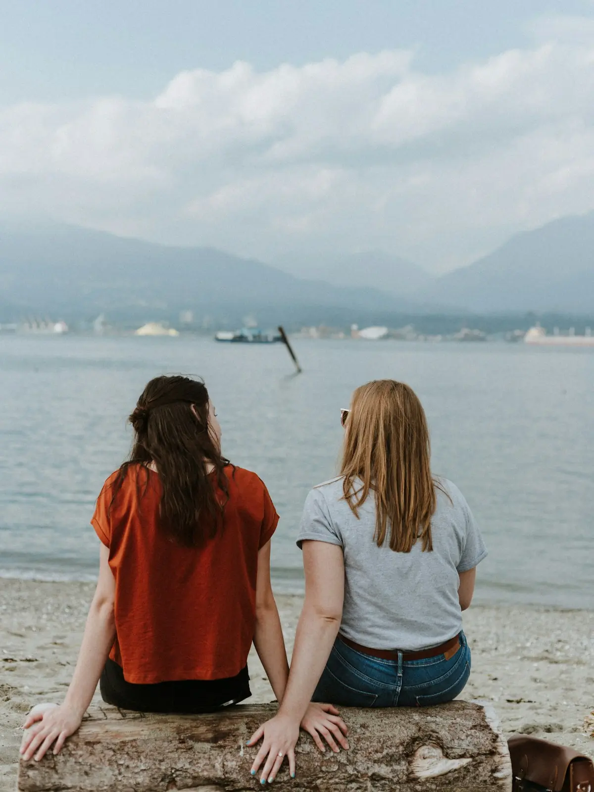 Two friends sitting together on a log by the sea, talking
