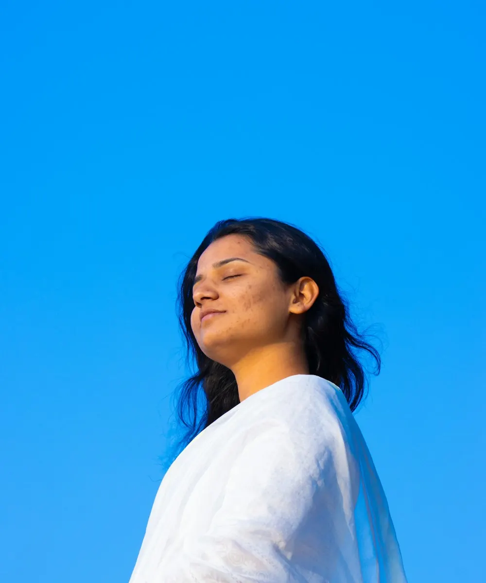 A young woman breathing calmly with her eyes closed under a clear blue sky
